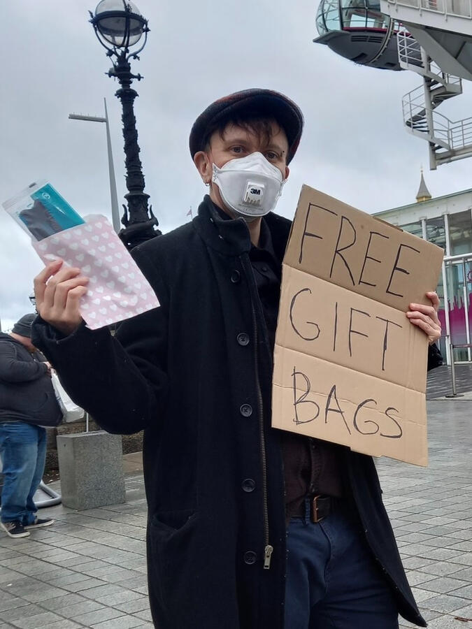 Protect the Heart of the Arts campaign member wearing a respirator giving away giftbag with respirator mask, Long Covid info card and awareness ribbon