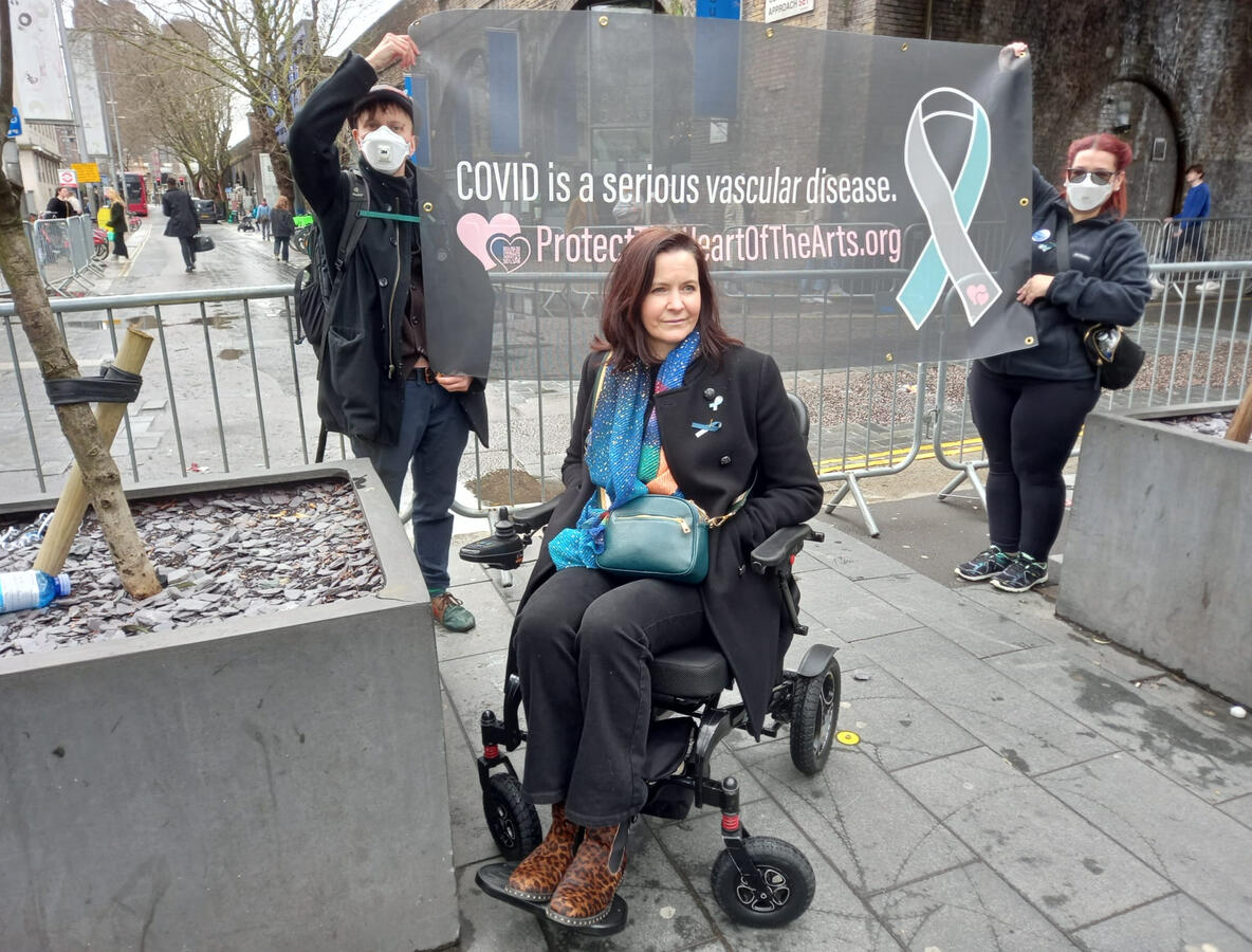 Protect the Heart of the arts campaign members and banner. Campaign member in power chair. Two others in respirator masks. Banner text: Covid is a serious vascular disease.